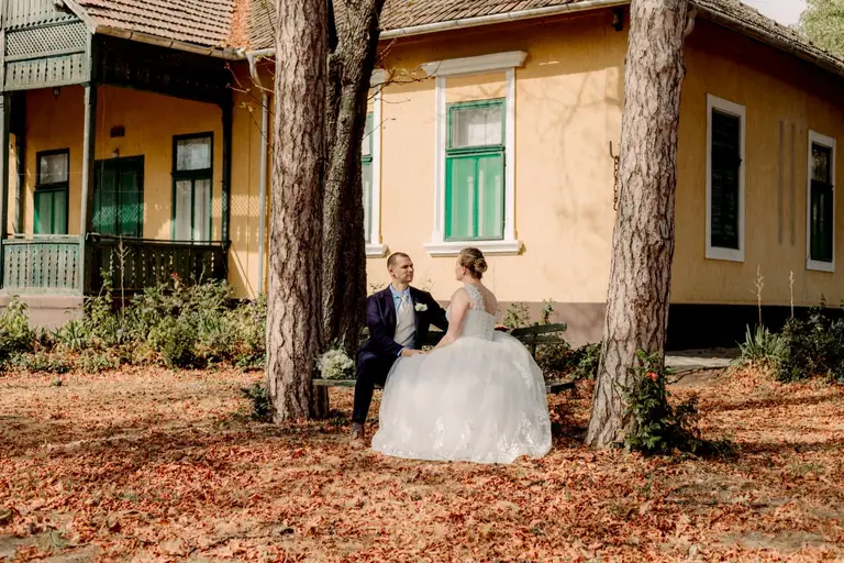 A pár a kúria előtti padon ül a fenyők alatt